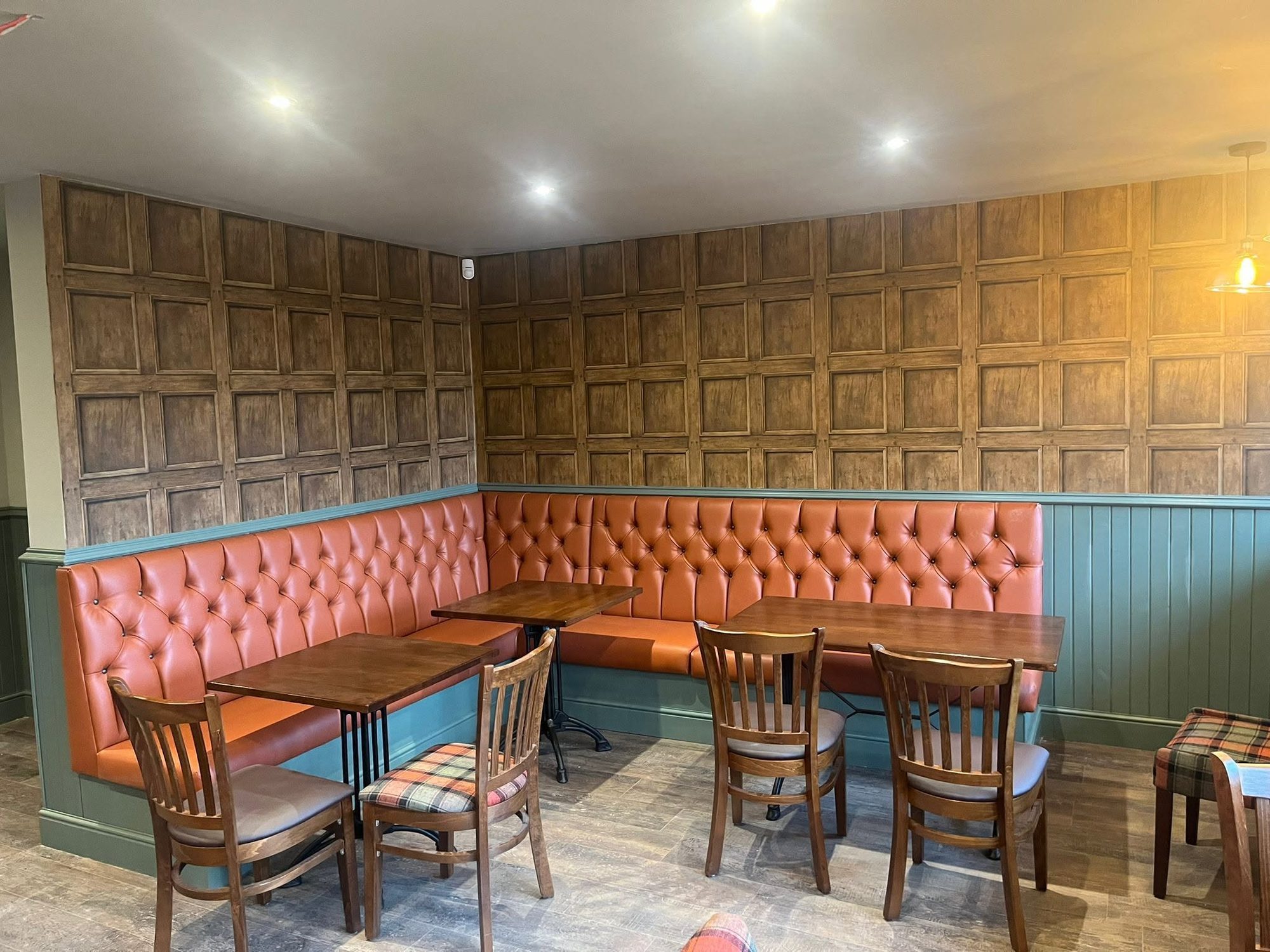 A bar booth corner with dark wood-panel-effect walls above sage panelling