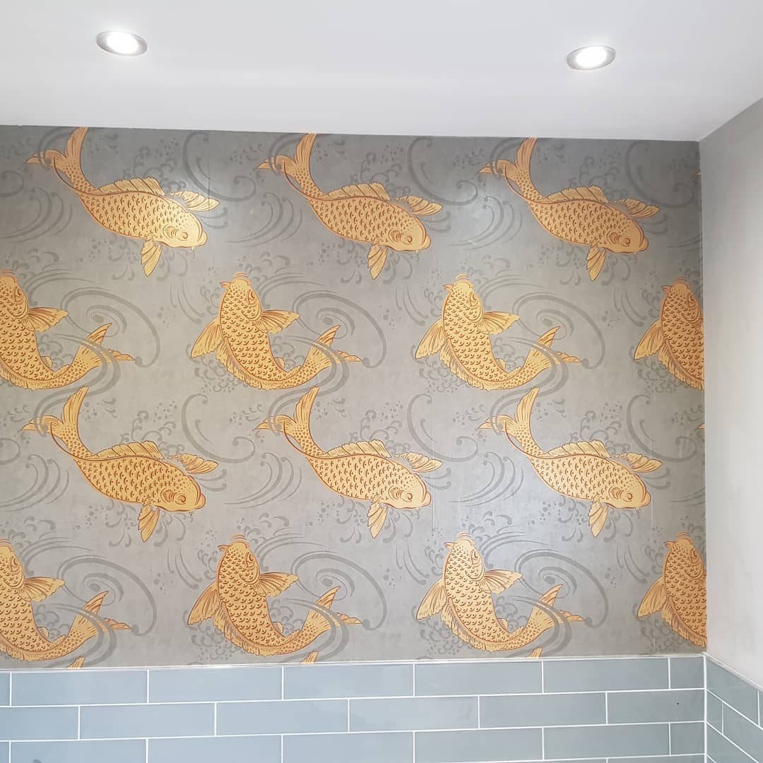 A feature wall papered in gold koi on grey, above blue-grey tiles