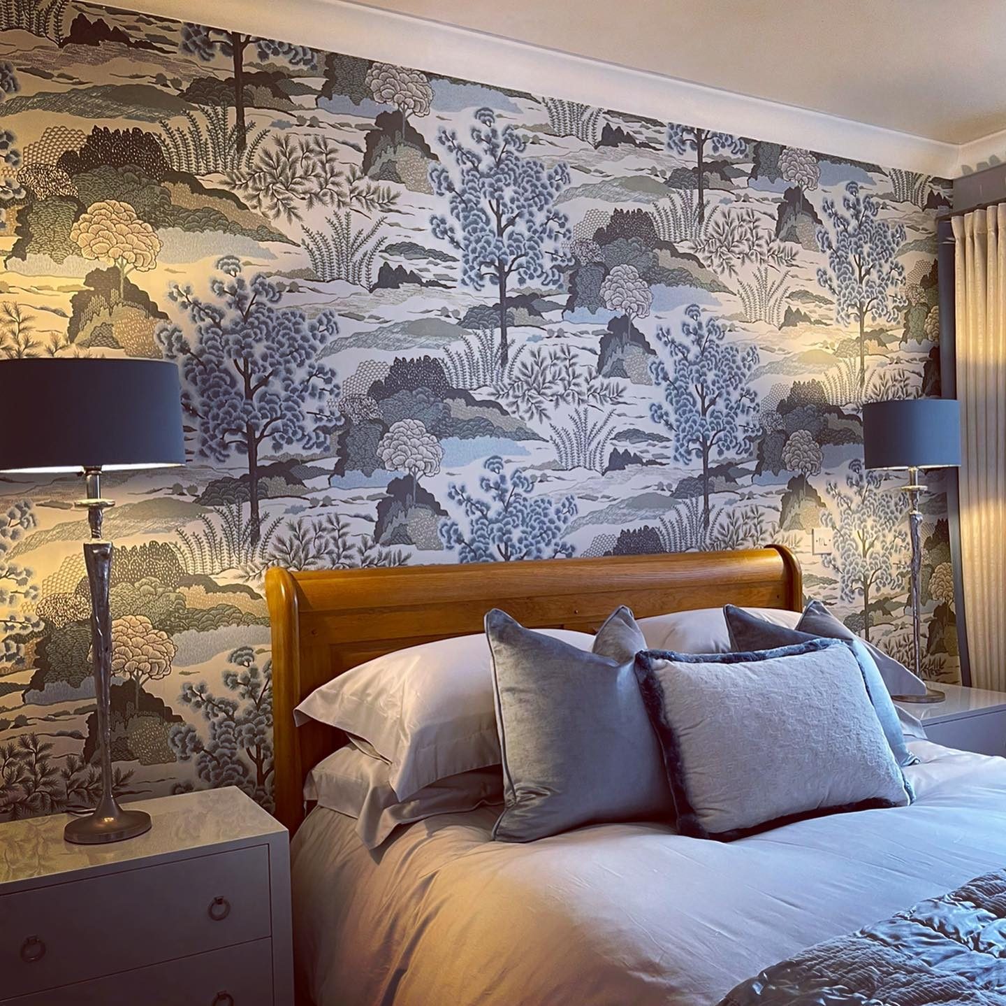 A bedroom feature wall papered in a blue and grey landscape print behind the bed