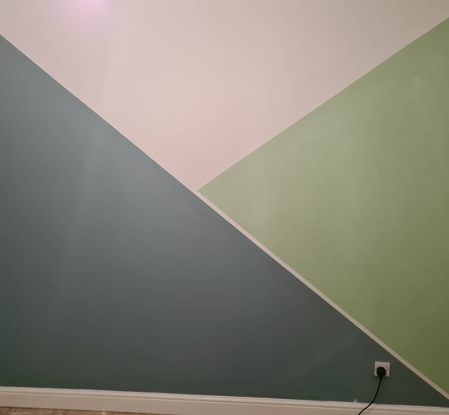A wall painted in large triangles of blue-grey, sage and blush, split by thin white lines