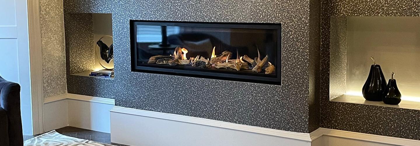 A chimney breast papered in a dark speckled paper round an inset fire, with lit shelf niches either side