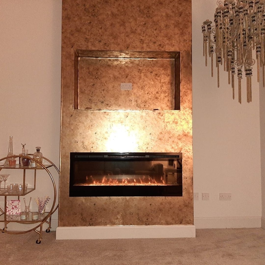 A chimney breast and recess covered in a copper-bronze metal-effect wall covering, over an inset fire