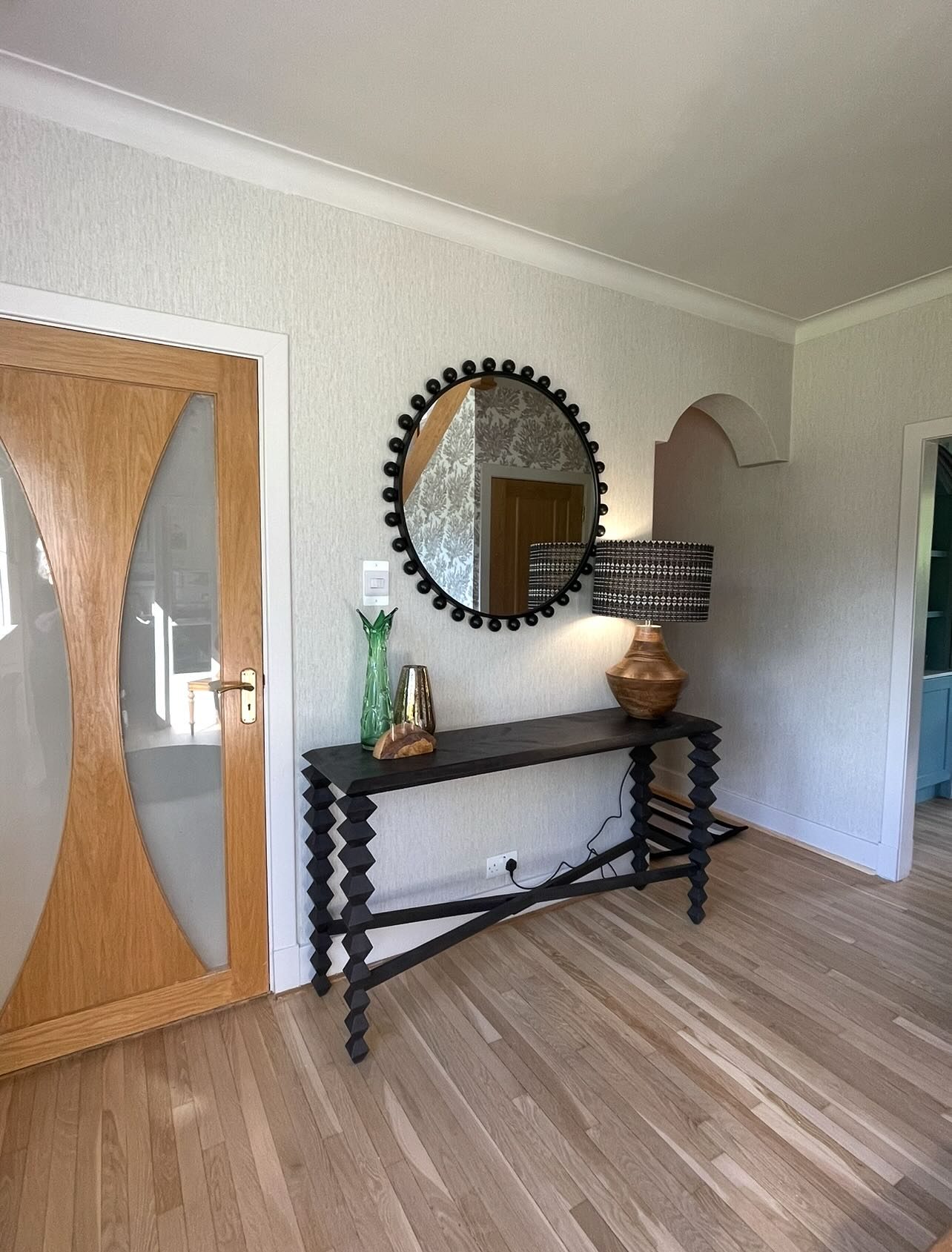 After: the same hall papered and redecorated, with a new door, a round mirror and a console