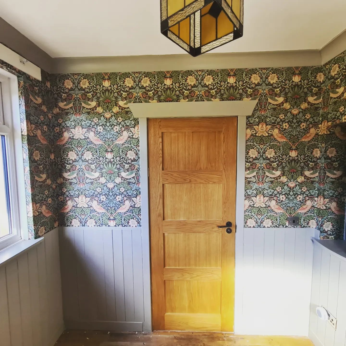 A small hallway papered in a dense bird-and-strawberry print, with an oak door