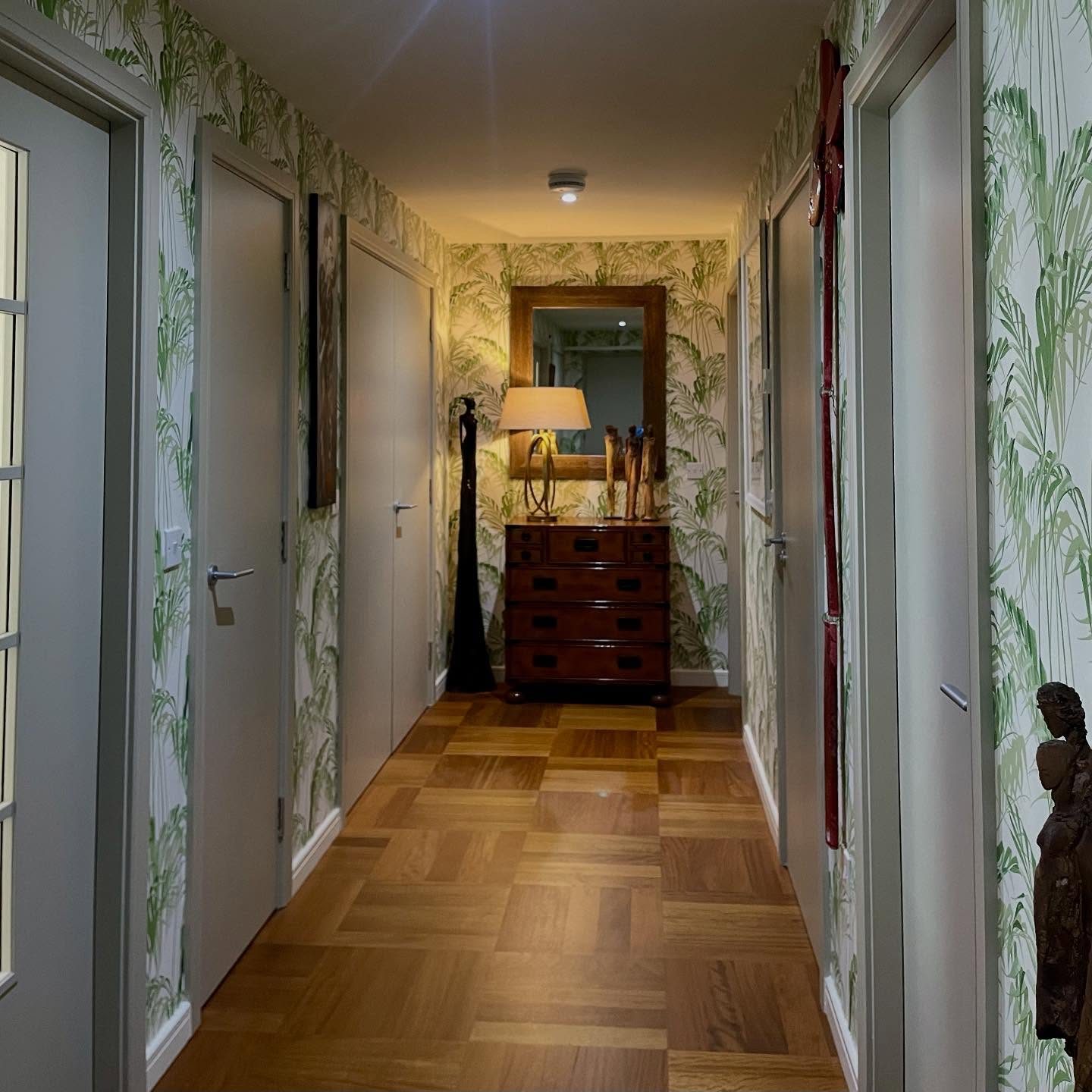 A long hallway papered in a green palm-leaf print
