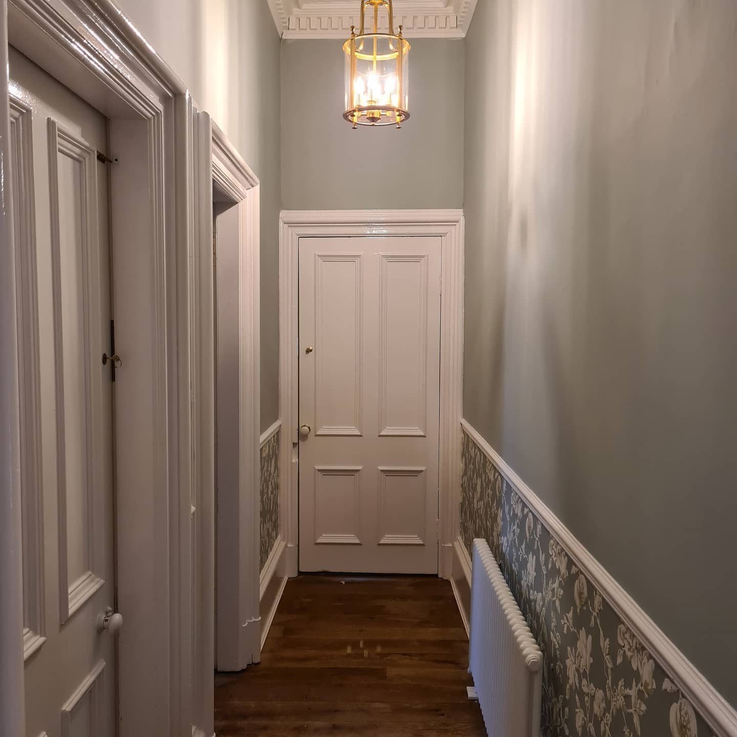 A long hallway with sage walls, white gloss doors and facings, and a floral paper below the dado