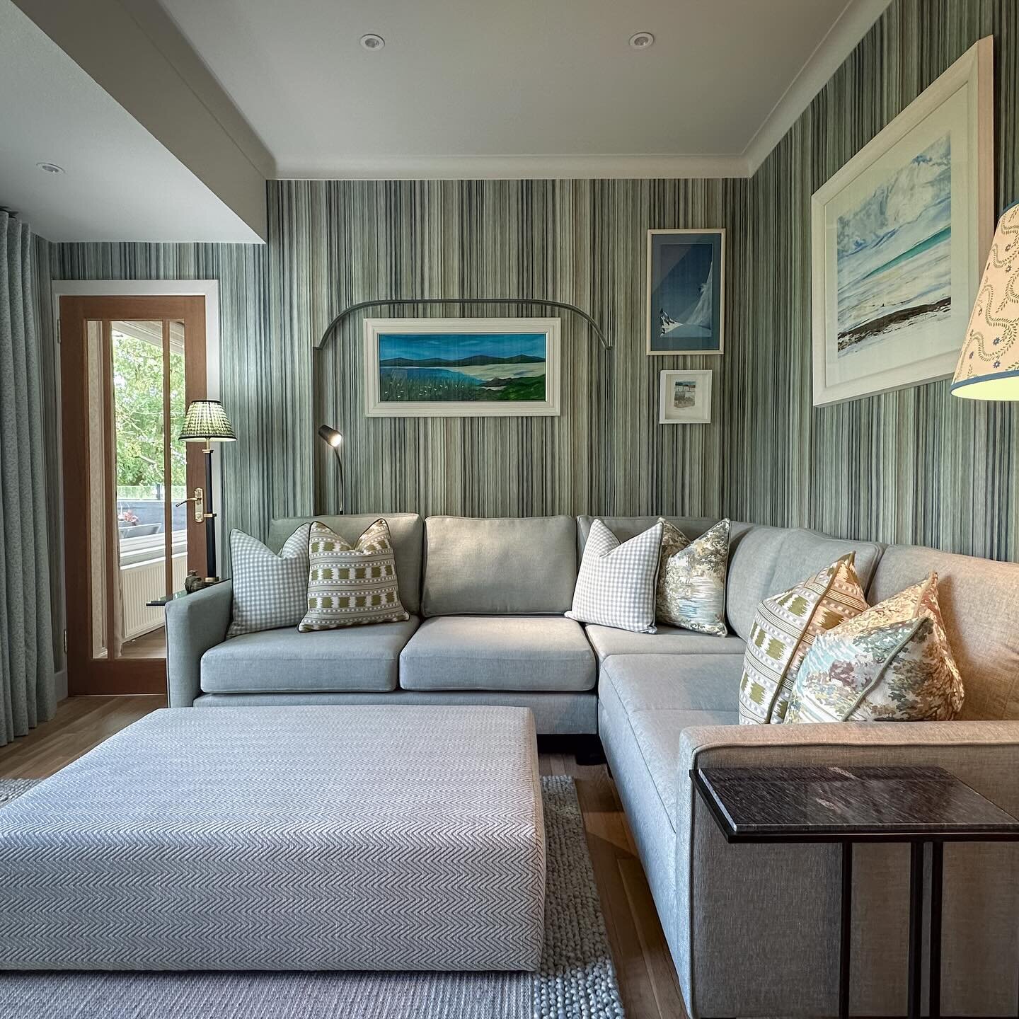 A lounge papered in a fine green, blue and grey stripe, behind a corner sofa