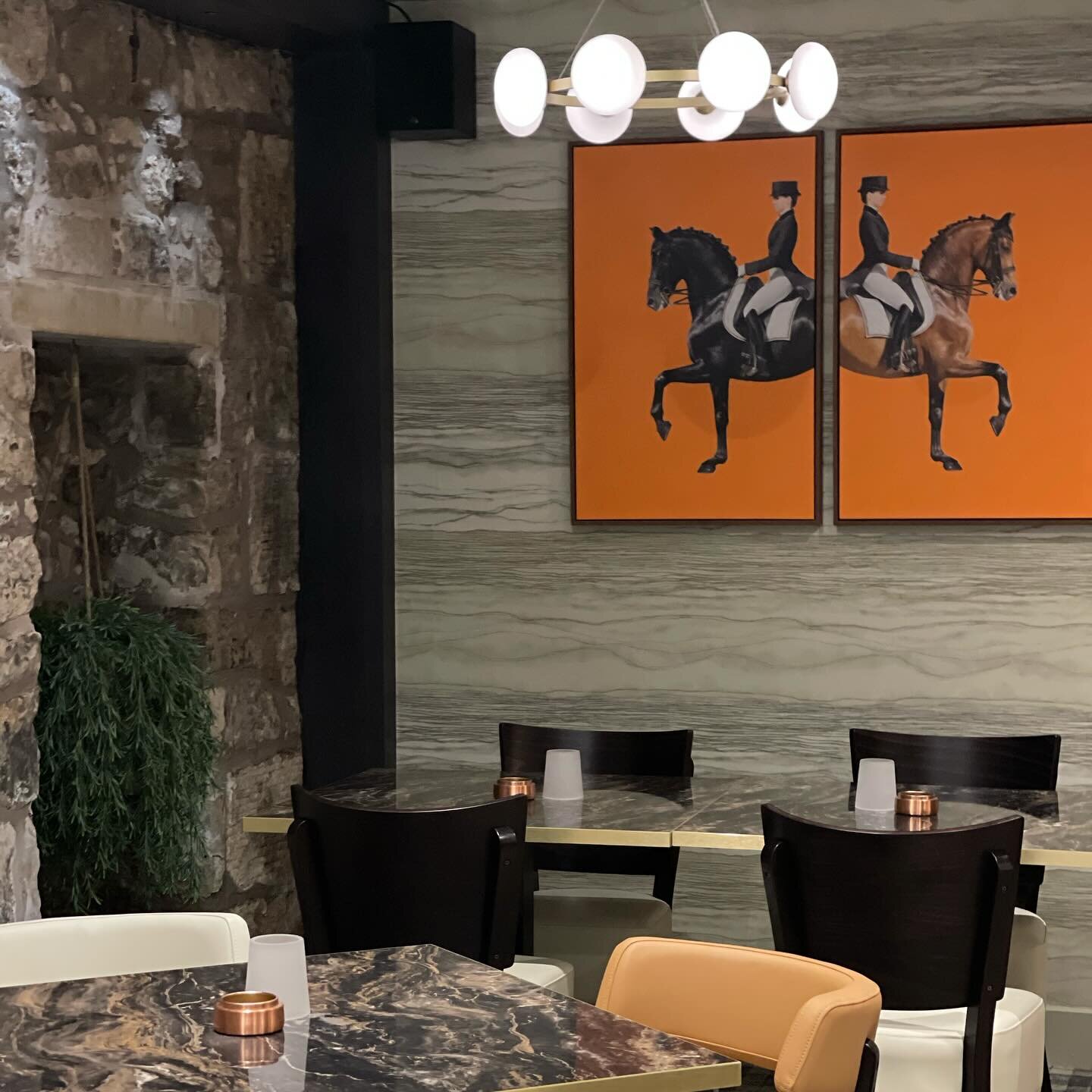 A bar restaurant wall papered in a grey stone-effect paper, behind two framed prints and dining tables