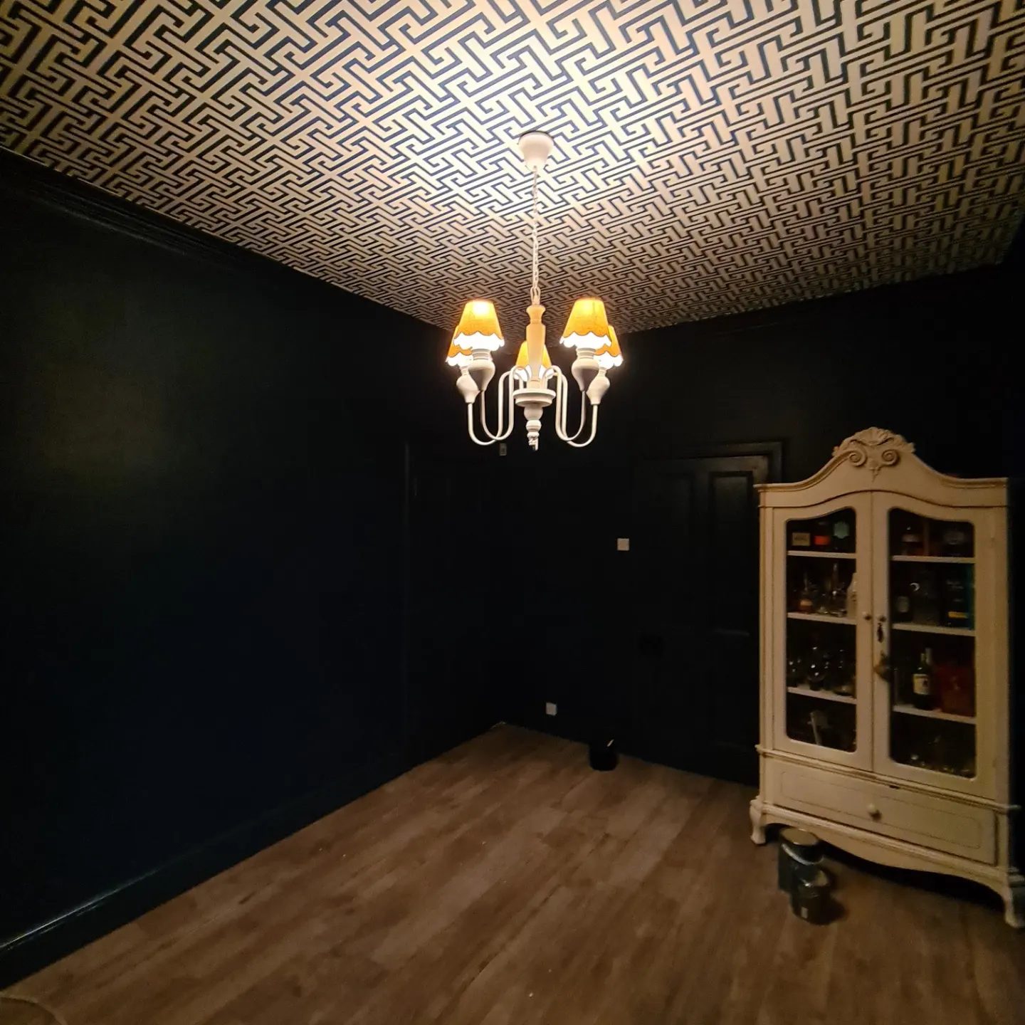 A dark room with a papered fret-pattern ceiling and a lit chandelier